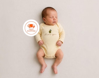 Peut inclure: Un body à manches longues pour bébé de couleur jaune pâle, orné d'une petite broderie représentant une olive verte sur la poitrine. Sous l'olive, le texte "olive you" est inscrit en écriture cursive brune. Il possède un col rond.