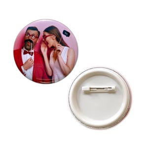 May include: A round button with a photo of a couple. The woman is whispering in the man's ear. The man is holding a fake mustache and the woman is holding a sign that says "his".