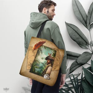 Może przedstawiać: Beżowa torba typu tote z ilustracją pirata w stylu vintage. Projekt zawiera portret pirata, czerwone pióro i tło mapy. Torba jest noszona na ramieniu.