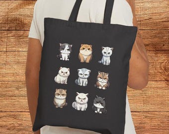 May include: Black tote bag featuring a pattern of nine cartoon cats in various colors and expressions. The cats are arranged in three rows of three, with a variety of fur patterns and facial expressions. The bag has black handles.