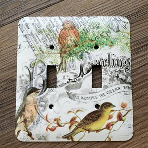 May include: A white light switch cover with a vintage design featuring birds, flowers, and the text "Little Darlings" and "Fly Across The Ocean Bird".