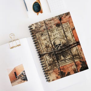 Könnte beinhalten: Spiralgebundenes Notizbuch mit einem Vintage-Design. Das Cover zeigt einen Totenkopf, eine Spinne und eine gealterte Papierstruktur mit dem Text "I Memorail Drill Treat Ne Road Battle Of". Das Notizbuch ist auf einer weißen Oberfläche geöffnet.