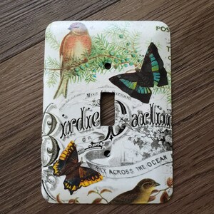 May include: A white light switch cover with a vintage design featuring a bird, butterflies, and the text "Gardine Pavilion" and "Fly Across The Ocean".