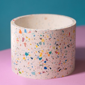 May include: A white cylindrical planter with a speckled terrazzo pattern in shades of pink, blue, green, yellow, and orange.