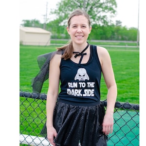 Puede incluir: Una mujer con una camiseta negra de tirantes con un gr&aacute;fico blanco de la cara de Darth Vader y el texto "Run to the Dark Side". Tambi&eacute;n lleva una falda de tul negra y una gargantilla negra.