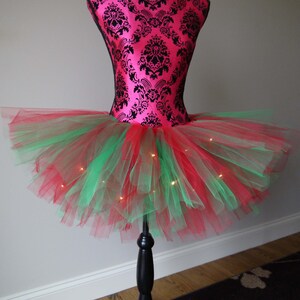 Puede incluir: Un tut&uacute; de tul rojo y verde con luces blancas. El tut&uacute; est&aacute; en un maniqu&iacute;.
