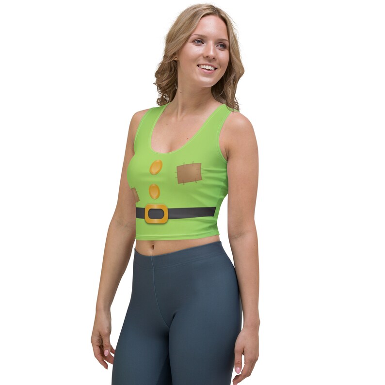 Puede incluir: Un top corto verde con un parche marr&oacute;n y un cintur&oacute;n negro con una hebilla dorada. El top tiene un dise&ntilde;o de dibujos animados del torso de un personaje.