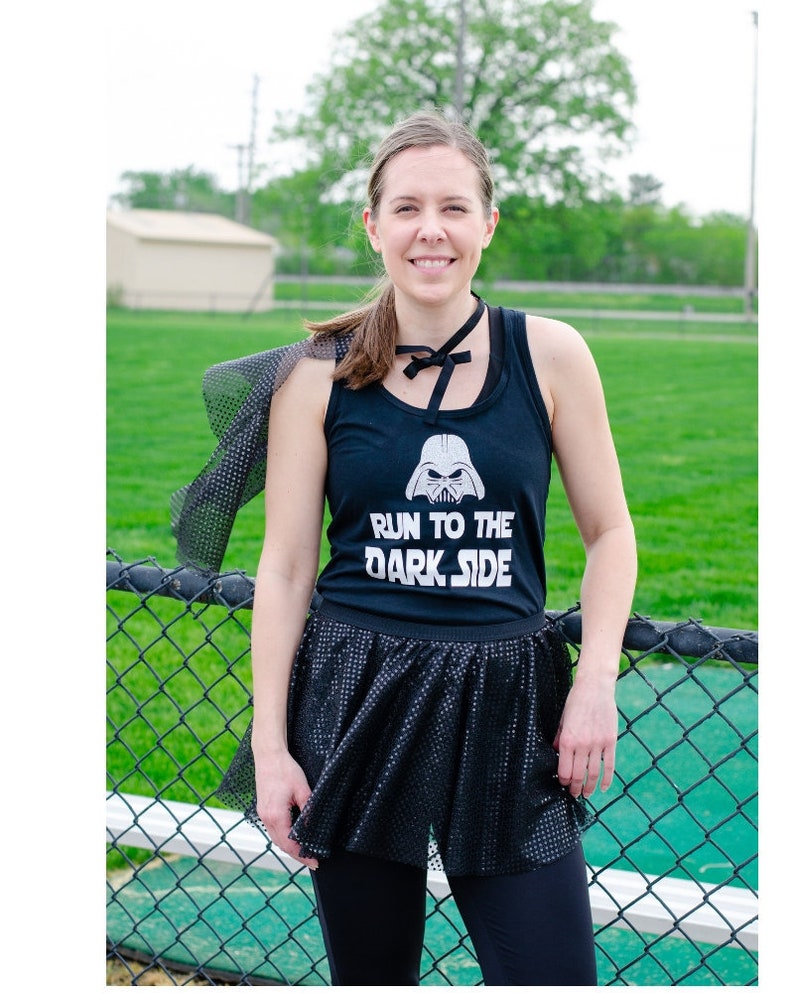 Puede incluir: Una mujer con una camiseta negra de tirantes con un gr&aacute;fico blanco de la cara de Darth Vader y el texto "Run to the Dark Side". Tambi&eacute;n lleva una falda de tul negra y una gargantilla negra.