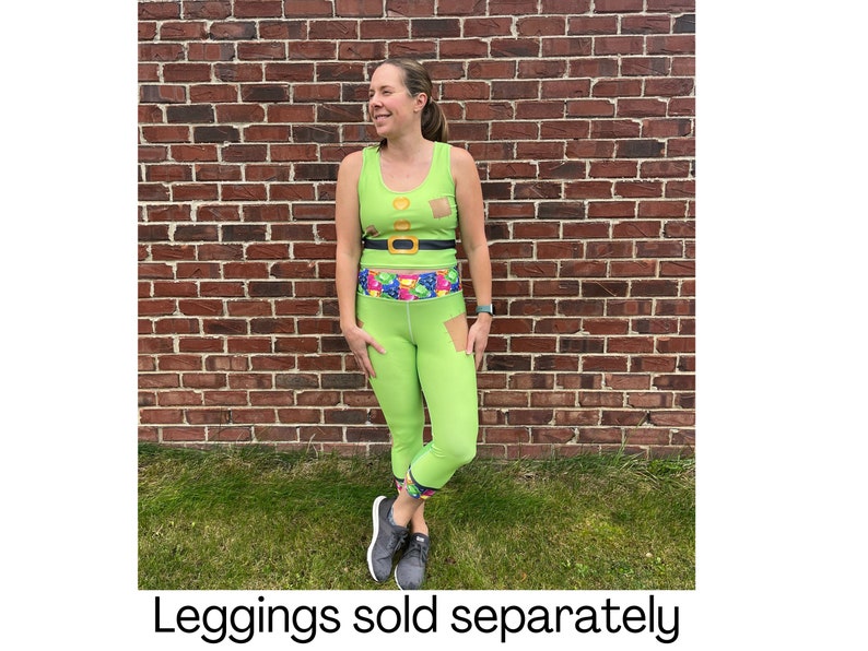 Puede incluir: Una mujer lleva un top verde sin mangas con un cintur&oacute;n dorado y un dise&ntilde;o estampado verde y blanco. Tambi&eacute;n lleva leggings verdes con una cintura colorida. Los leggings son cortos y tienen un peque&ntilde;o desgarro en la pierna izquierda. El texto "Leggings vendidos por separado" est&aacute; en la parte inferior de la imagen.