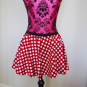 May include: A red skirt with white polka dots and a black waistband. The skirt is on a mannequin with a pink and black patterned bodice.