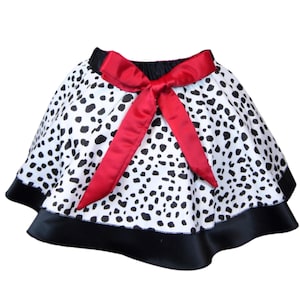 Puede incluir: Una falda de estampado dálmata blanco y negro con un lazo de satén rojo y ribete de satén negro.