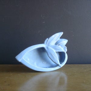Könnte beinhalten: Eine hellblaue Keramik Schale in Form einer Blume mit einem einzelnen Blatt und drei Blütenblättern. Die Schale ist dazu bestimmt, kleine Gegenstände wie Schmuck oder Nippes aufzunehmen.