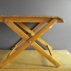 May include: A wooden folding table with a natural wood finish. The table is made of multiple pieces of wood that are joined together to form a sturdy and functional piece of furniture.