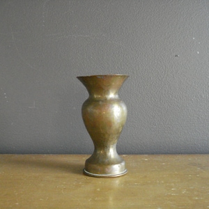 May include: A small, brass vase with a hammered finish. The vase has a rounded base and a narrow neck.