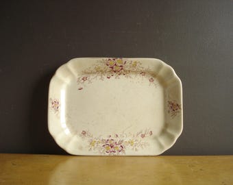 May include: A white ceramic serving tray with a scalloped edge and a floral design in shades of yellow, pink, and brown.