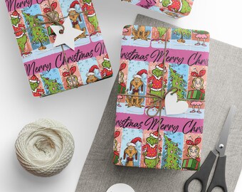 May include: Christmas-themed gift wrap featuring cartoon characters in a colorful grid pattern. The wrapping paper has a pink border with the words "Merry Christmas" and is tied with twine and a star-shaped tag. A ball of twine, scissors, and tags are also present.