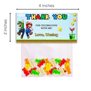 May include: A thank you favor bag with a Mario and Luigi design. The bag is 4 inches wide and 2 inches tall. The bag has a printed label that says "Thank You for celebrating with me! Love, Wesley". The bag is filled with colorful gummy candies.