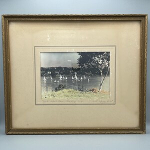 May include: A framed vintage print depicting sailboats on a lake. The artwork is a black and white image with colour accents, set within a gold-toned ornate frame. The scene includes a tree and a shoreline.