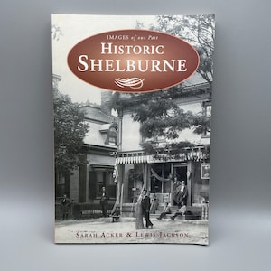 Peut inclure: Une couverture de livre avec un ovale brun contenant le texte "Historic Shelburne" en lettres blanches. La couverture du livre présente une photographie en noir et blanc d'une scène de rue avec un groupe de personnes debout devant un bâtiment. Le texte "Images of our Past" est imprimé au-dessus de l'ovale. Le texte "Sarah Acker & Lewis Jackson" est imprimé en dessous de l'ovale.