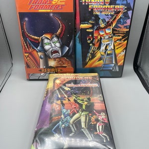 Op de afbeelding: Drie VHS-banden van de Transformers-tekenfilmserie. De banden zijn getiteld "The Transformers: The Movie", "Transformers: Generation 2: Rebirth" en "Transformers: War of the Dinobots".