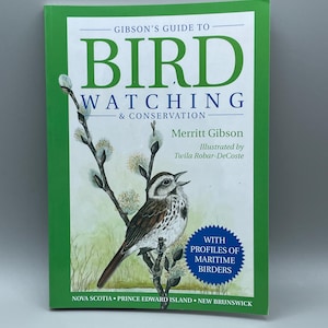 May include: A hardcover book titled "Gibson's Guide to Bird Watching & Conservation." The cover features a detailed illustration of a bird perched on a branch with white flowers. The book has a green border and includes text about maritime birders.