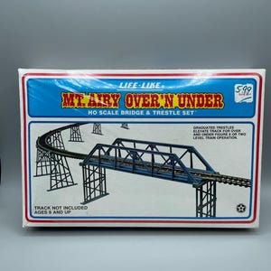 May include: A boxed HO scale bridge and trestle set labelled "Mt. Airy Over 'N Under" with a blue and red border. The box art depicts a model train bridge and trestle system. Text on the box includes "Track Not Included" and "Ages 8 and Up."