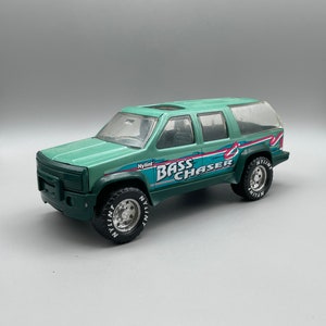 May include: A green toy truck with a white "Bass Chaser" graphic on the side. The truck has a black grille and black tyres with white lettering.