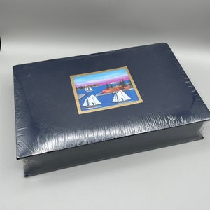 May include: A black photo album with a gold trim and a colourful image of sailboats on a lake. The image is framed with a gold border.