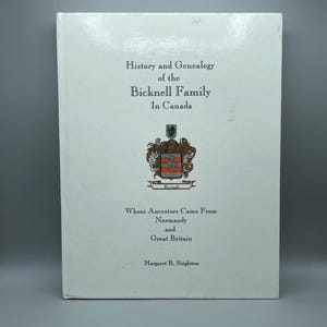 Puede incluir: Una cubierta de libro blanca con el título "Historia y genealogía de la familia Bicknell en Canadá" y el subtítulo "Cuyos antepasados vinieron de Normandía y Gran Bretaña". La autora es Margaret R. Singleton.