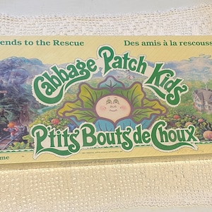 Op de afbeelding: Een gele speldoos met een groen Cabbage Patch Kids-logo en de tekst "Friends to the Rescue" en "Des amis à la rescousse". De doos heeft een cartoonafbeelding van een Cabbage Patch Kid.