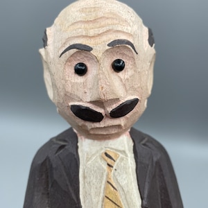 May include: A wooden figurine of a man with a moustache and a tie. He is wearing a brown suit jacket and has a serious expression on his face.