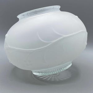 May include: A frosted glass lamp shade with a rounded, bulbous shape featuring an embossed leaf and vine pattern. The top opening has a smooth rim, while the base features a clear, ribbed glass collar with a sunburst pattern on the bottom edge.