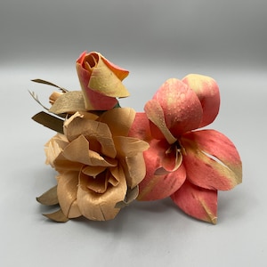 May include: A cluster of three artificial flowers made of wood. The flowers are in shades of pink and beige. The flowers are arranged in a bouquet.