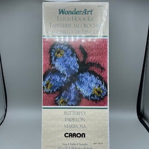 Könnte beinhalten: Ein Latch-Hook-Set mit einem Schmetterlingsmotiv in blau, gelb und rosa Garn. Das Set enthält Anleitungen und Garn, um eine 30,4 cm x 30,4 cm große Wandteppich zu erstellen. Die Schachtel ist mit "WonderArt" und "CARON" beschriftet.