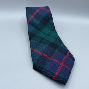 May include: A plaid necktie in shades of navy blue, green, and black, with thin red stripes. The tie is angled, showcasing the pattern and texture of the fabric. The classic design is suitable for formal or business attire.