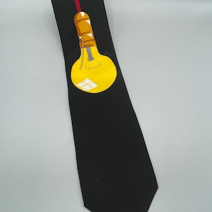 May include: Black tie with a yellow lightbulb design. The lightbulb has a yellow bulb, a gold base, and a red accent stripe. A classic accessory for formal or business wear, suitable for various occasions.