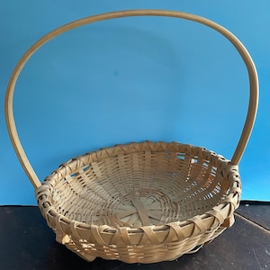 May include: A woven wicker basket with a single, rounded handle. The basket is light brown and has a natural, rustic look.