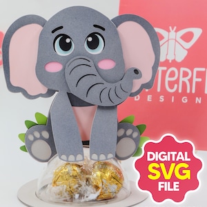 Puede incluir: Un recorte de papel gris con forma de elefante con orejas internas rosas y una trompa, sentado sobre un recipiente de plástico transparente lleno de bombones envueltos en oro. El diseño incluye detalles de hojas verdes y el texto "DIGITAL SVG FILE" y "SAFARI COLLECTION".