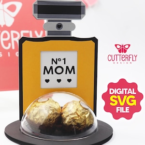 May include: A decorative perfume bottle-shaped gift box with the text "N°1 MOM" and three heart symbols. The box is yellow and black, with a clear dome containing two gold-wrapped chocolates. The design includes the "Cutterfly Design" logo and a "DIGITAL SVG FILE" badge.