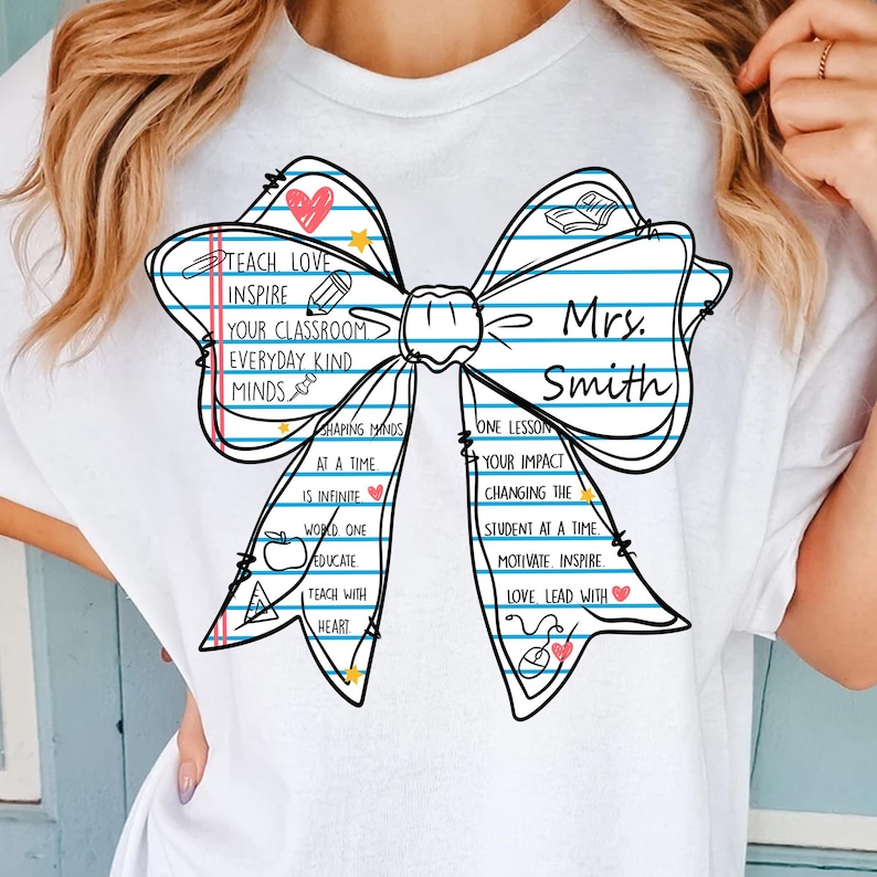 May include: White t-shirt featuring a bow design with lined paper texture and the words "Teach Love Inspire" and "Mrs. Smith". The bow includes hearts, stars, and school-themed illustrations. A personalized gift for teachers.