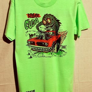 May include: Lime green t-shirt with a graphic of a monster driving a red car with flames. The text "Killer Cuda" is above the car, and "Zercie" is printed at the bottom. The monster has large eyes and sharp teeth.
