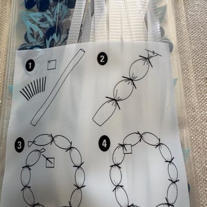 May include: A clear plastic package containing white ribbons and a printed instruction sheet with four numbered steps. The diagrams illustrate a process for tying ribbons into a circular shape, featuring black line drawings of tubes, knots, and loops.