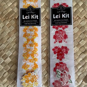 May include: Two Island Heritage Lei Kits in clear plastic packaging. The left kit features orange and white floral patterns with matching tags, measuring 2.75 inches by 52 inches. The right kit has red and white hibiscus designs with tags, measuring 2.75 inches by 59 inches.