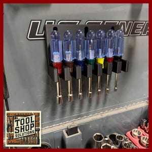 May include: A black metal tool holder with seven screwdrivers. The screwdrivers have clear blue handles and silver shafts. The handles are capped with red, brown, and yellow. The image also shows the text "TOOL SHOP SOLUTIONS".