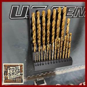 May include: A set of gold-colored drill bits in a black organizer. The drill bits are arranged vertically, with sizes labeled at the bottom. The image includes the text "TOOL SHOP SOLUTIONS".
