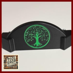 May include: A black, semi-circular tool with a green tree of life design. The tree is in a circular frame. The tool has a logo that says "TOOL SHOP SOLUTIONS".