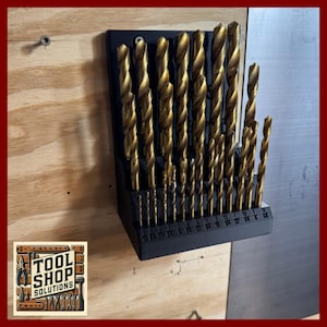May include: A set of gold-colored drill bits in a black holder, mounted on a light wood surface. The drill bits are of varying sizes, with measurements printed on the holder. The Tool Shop Solutions logo is visible in the lower left corner.