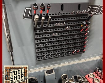 Puede incluir: Organizador de herramientas negro con múltiples agujeros, que contiene varias herramientas con detalles en rojo y plateado. El organizador está montado sobre una superficie gris. La imagen también muestra un logotipo de "Tool Shop Solutions".