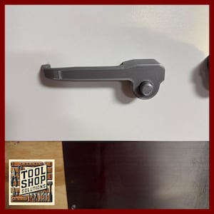 May include: A gray, 3D-printed door handle with a textured surface. The handle has a curved lever and a circular knob. The handle is mounted on a white surface.