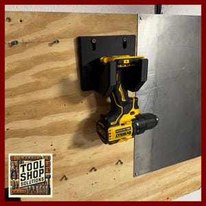 May include: A black drill holder mounted on a wooden surface, holding a yellow and black DeWalt 20V drill. The holder is attached to a wooden panel and a metal sheet. The Tool Shop Solutions logo is in the lower left corner.